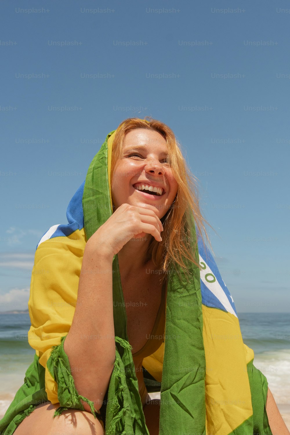 a woman sitting on the beach with a towel around her neck