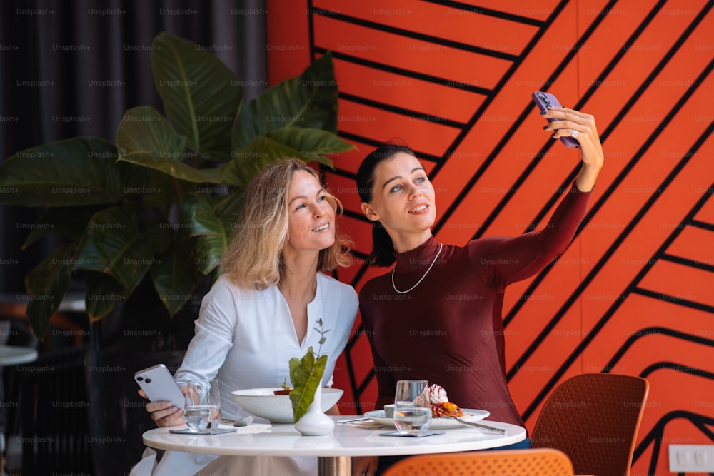 duas mulheres sentadas em uma mesa tirando uma selfie