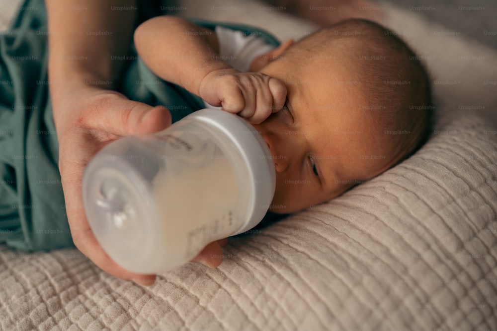 a baby drinking from a bottle while laying on a bed