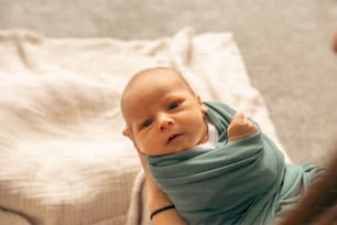 ein Baby, das in eine Decke gewickelt auf einem Bett sitzt