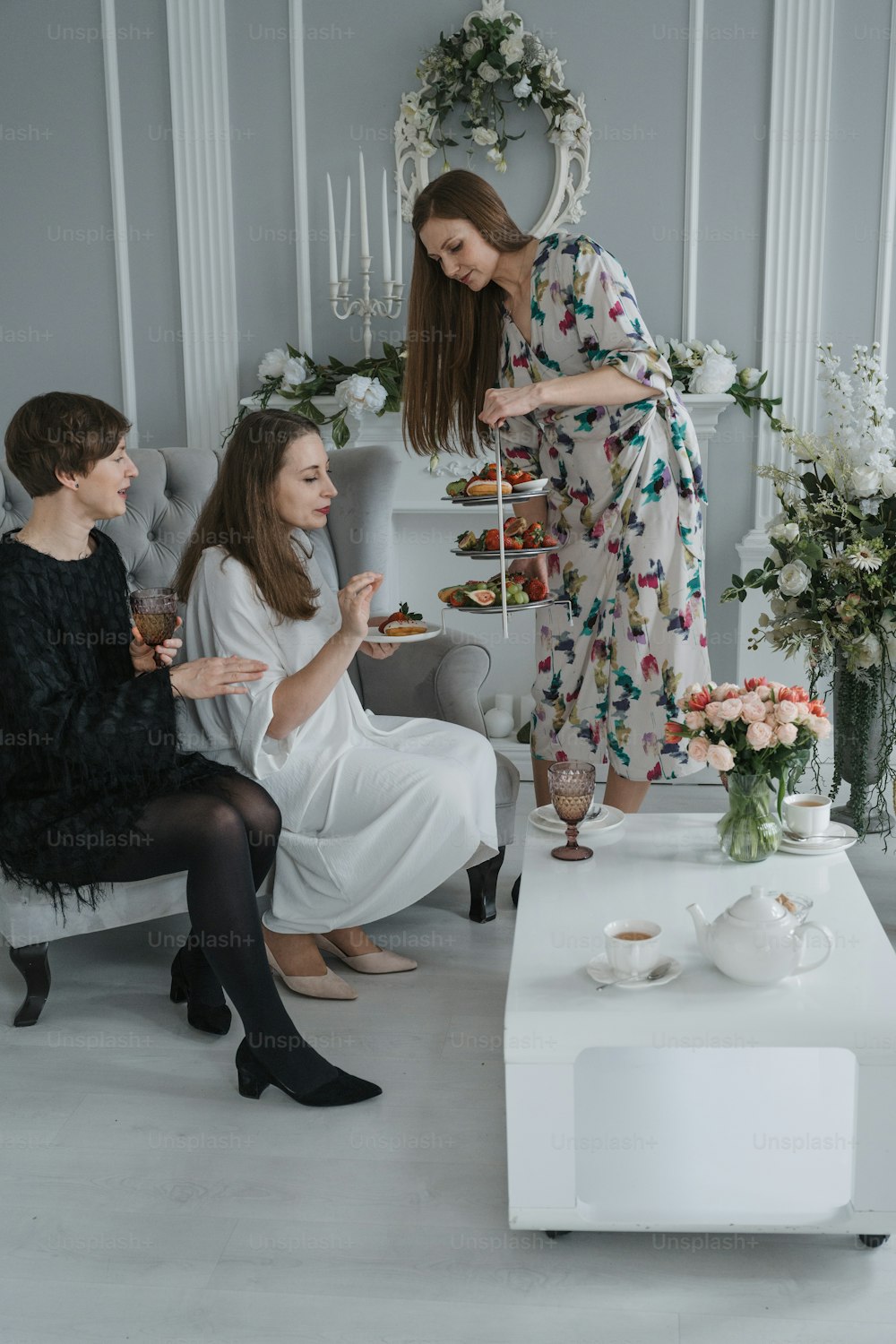a woman in a floral dress is serving tea to two other women