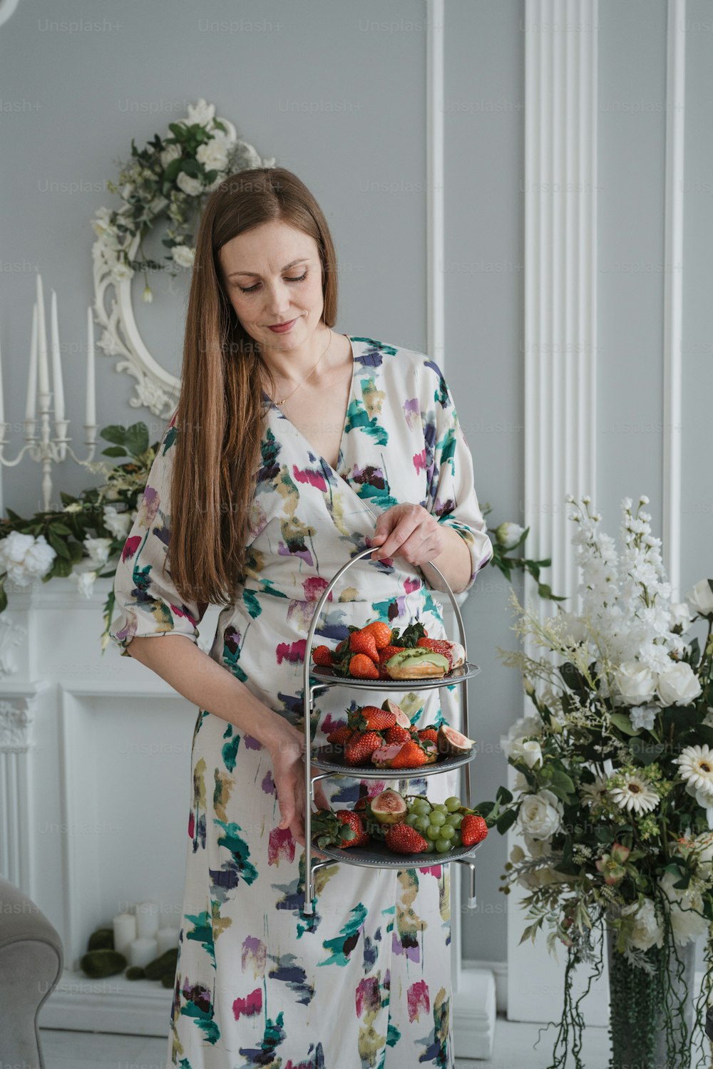 a woman in a floral dress holding a tray of fruit