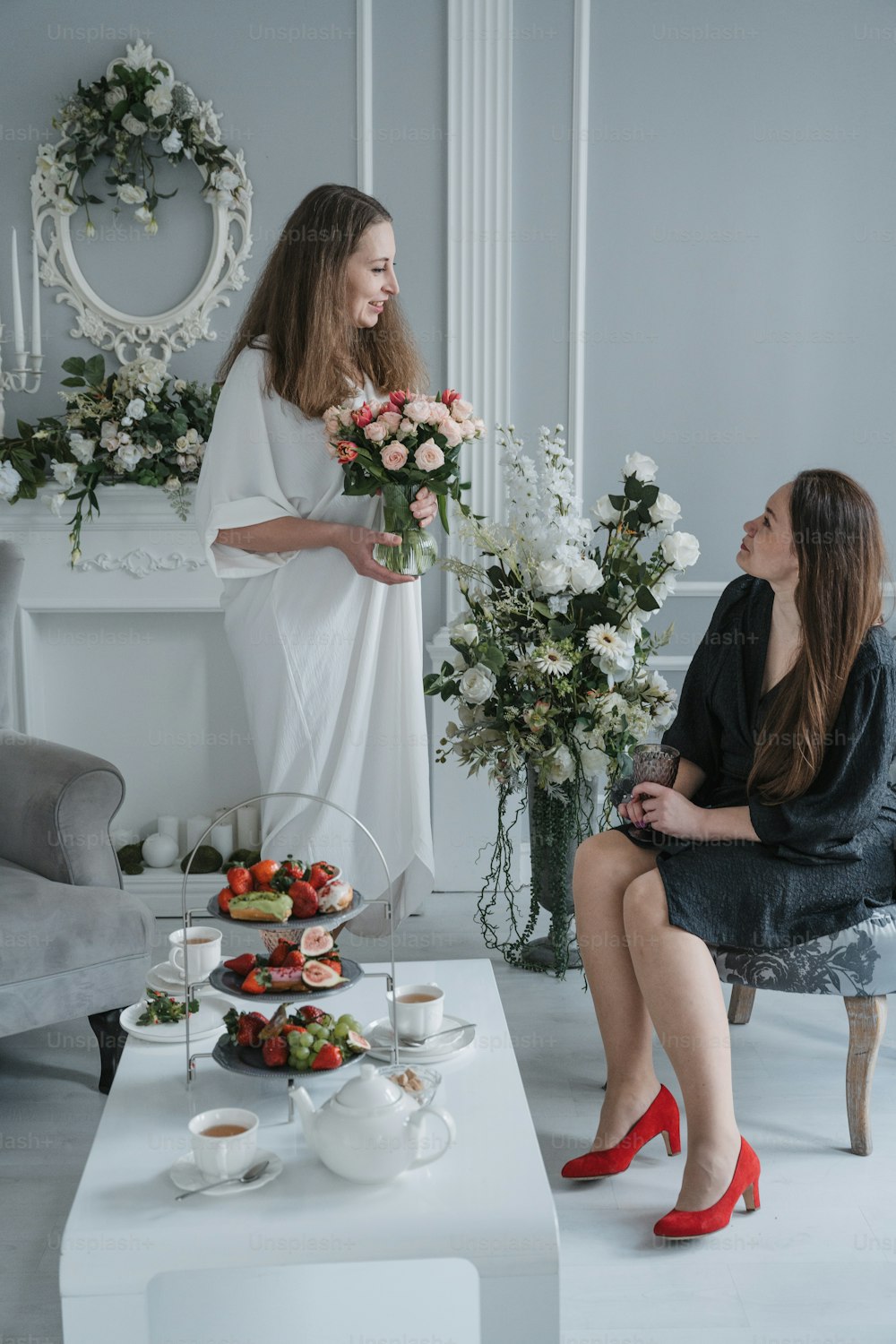 two women sitting on a couch in front of a table with flowers