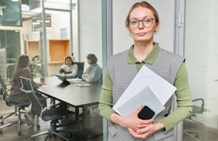 a woman standing in an office holding a piece of paper
