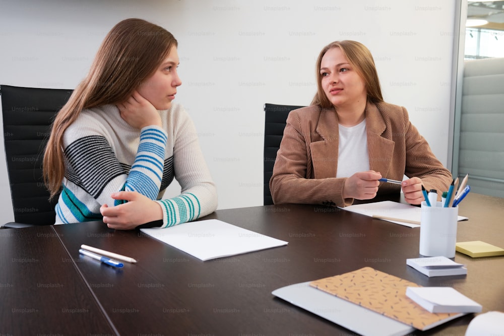 two women sitting at a table with notebooks and pens