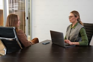 two women sitting at a table with laptops