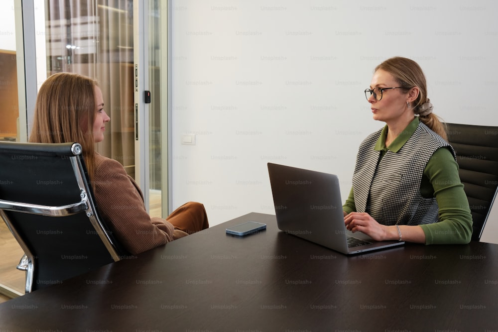 two women sitting at a table with laptops