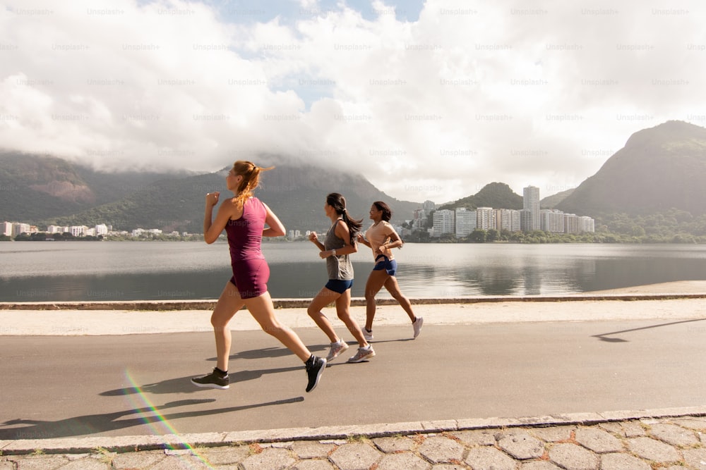 a group of women running on a road next to a body of water