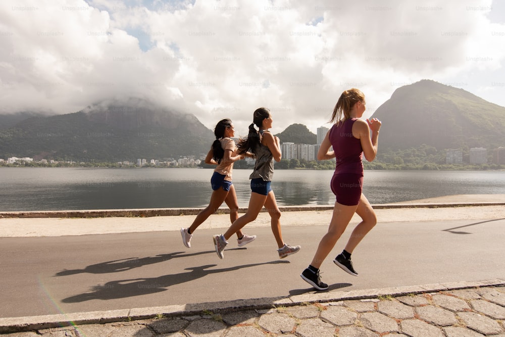 a group of women running on a road next to a body of water