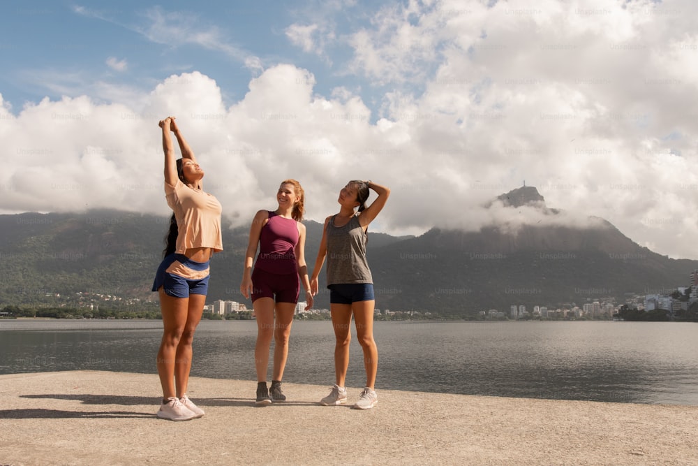 three women are standing on the edge of a body of water