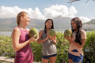 a group of women holding up coconuts in front of a body of water