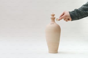 eine Person, die eine Münze in eine Vase legt
