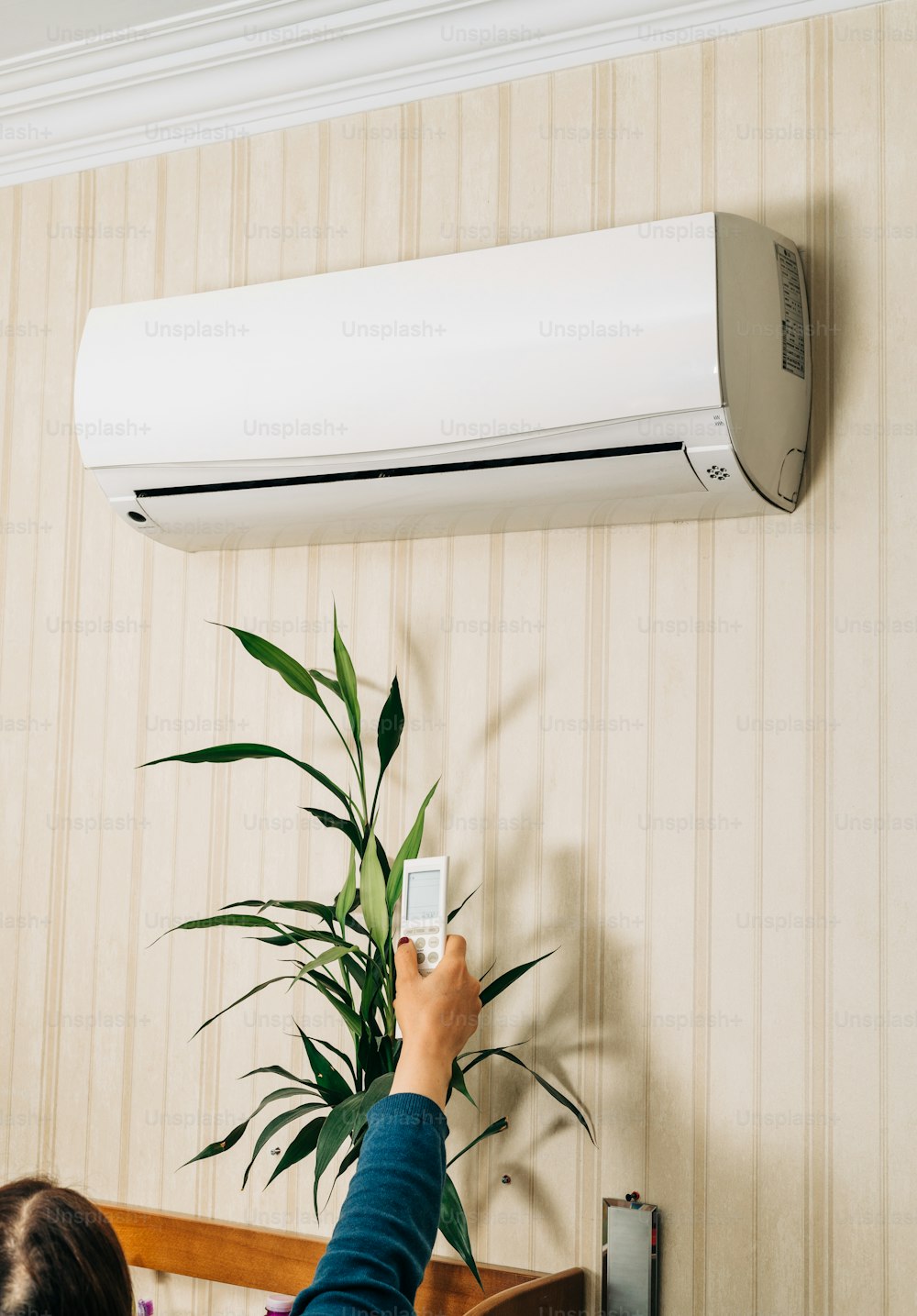 a person holding a remote control in front of a wall mounted air conditioner