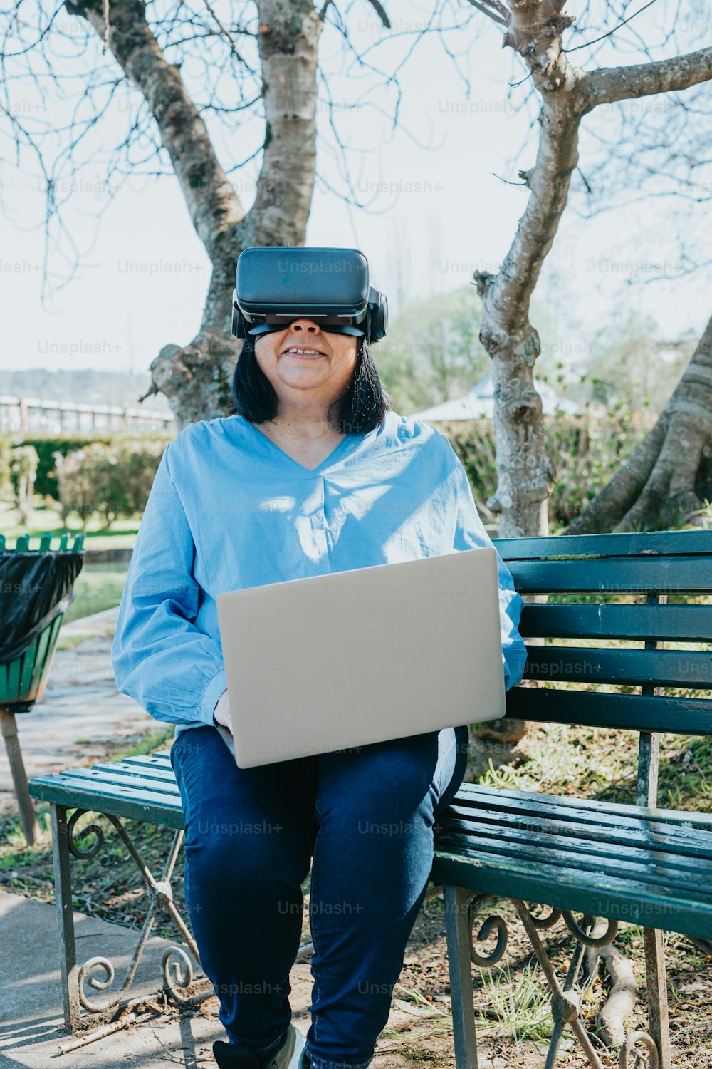 a woman sitting on a bench with a laptop wearing a virtual headset