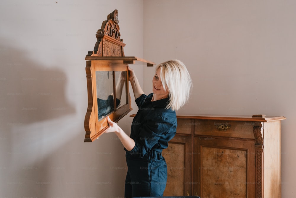 a woman holding a clock in front of a dresser