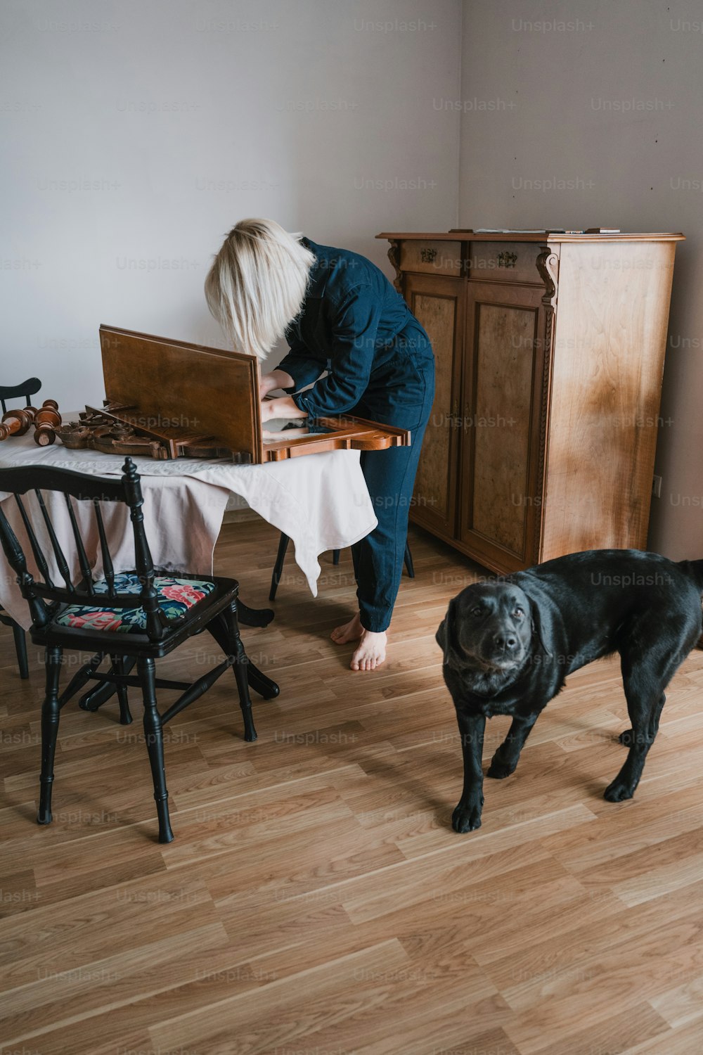 a woman standing next to a black dog on a hard wood floor
