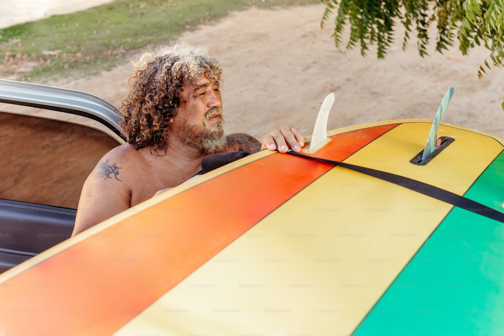 Un hombre con el pelo largo sentado en un coche sosteniendo una tabla de surf