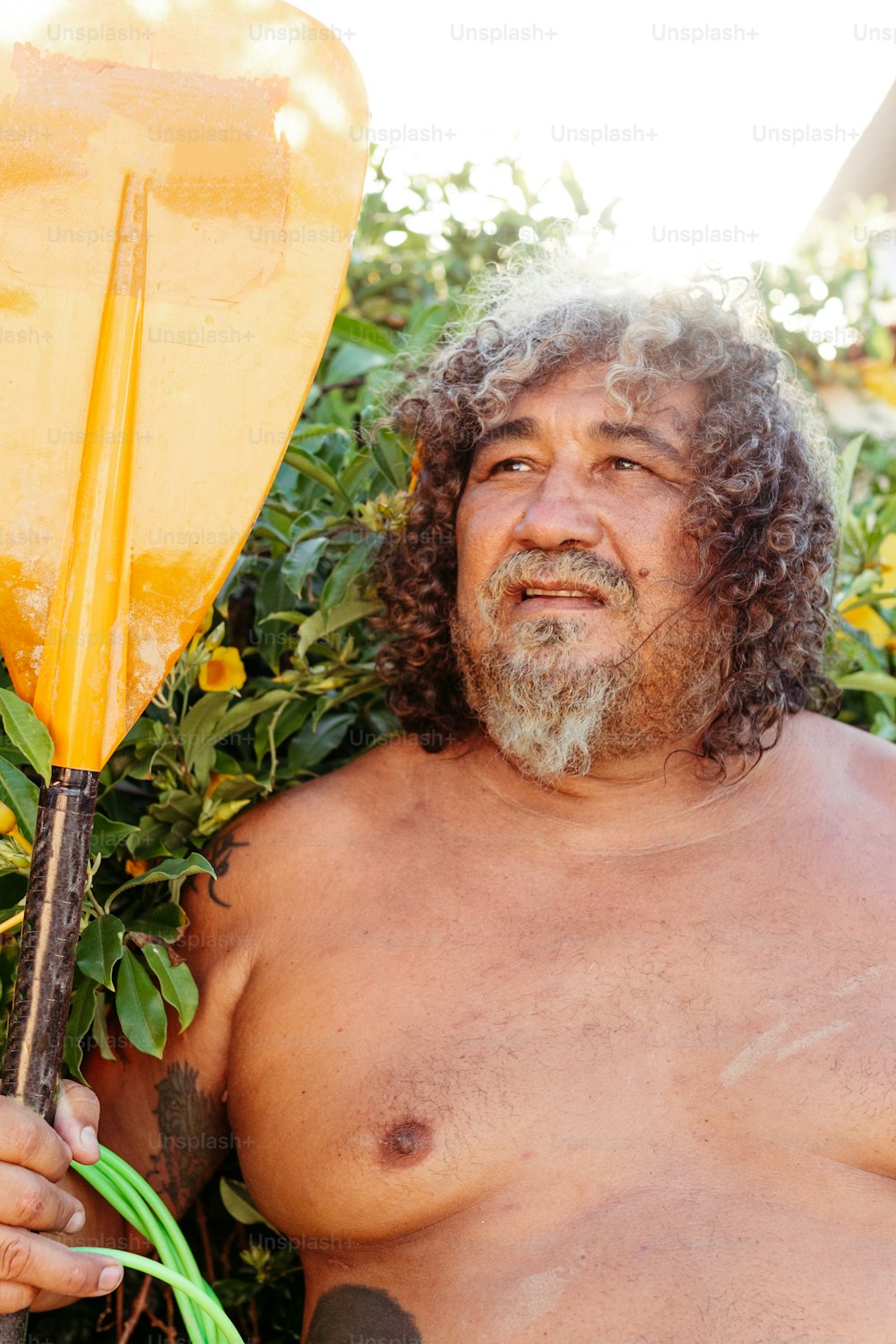 Un uomo a torso nudo che tiene una grande pagaia gialla