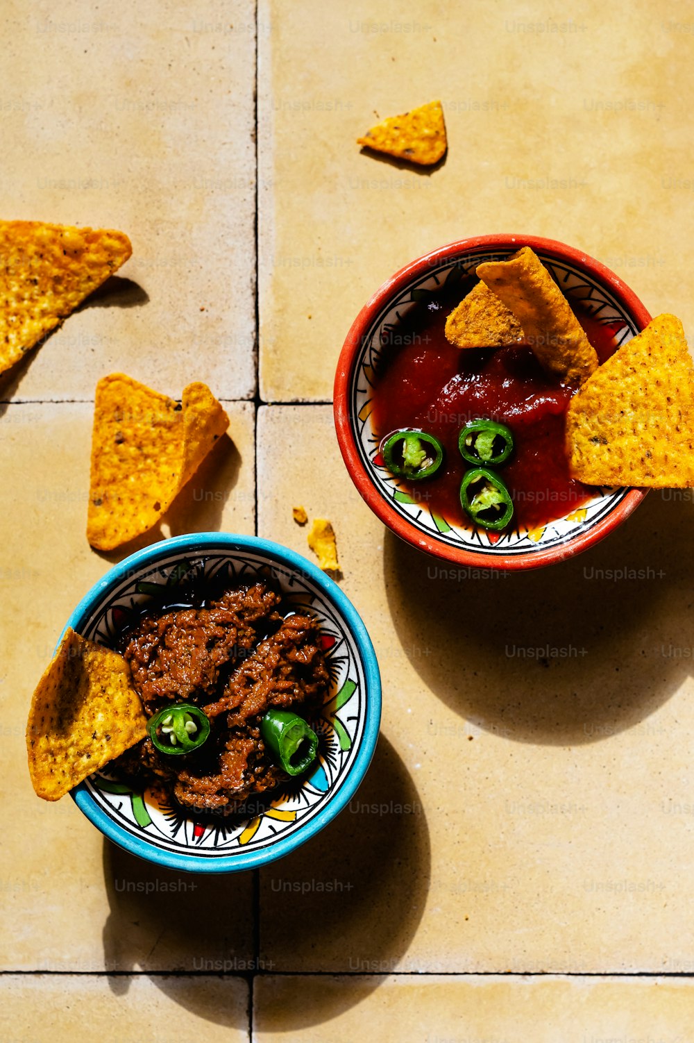 two bowls of chili and tortilla chips on a tile floor