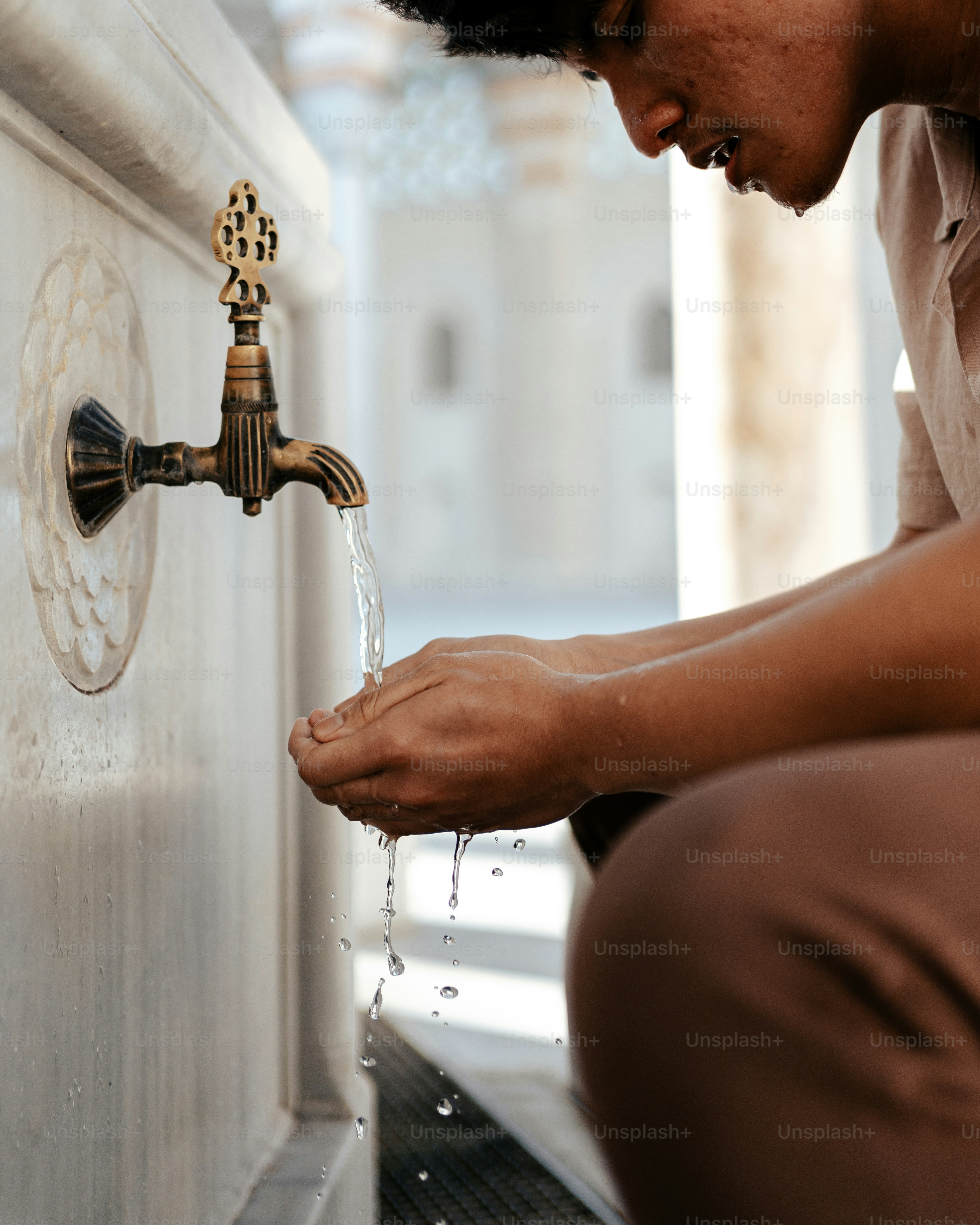 Ein Mann sitzt auf dem Boden und trinkt Wasser aus einem Wasserhahn