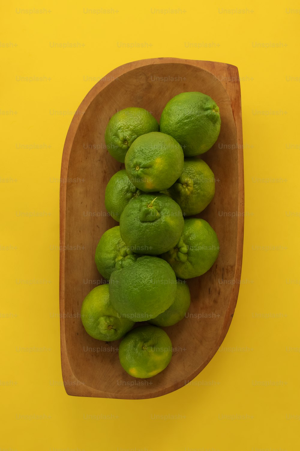 a wooden bowl filled with green fruit on a yellow background