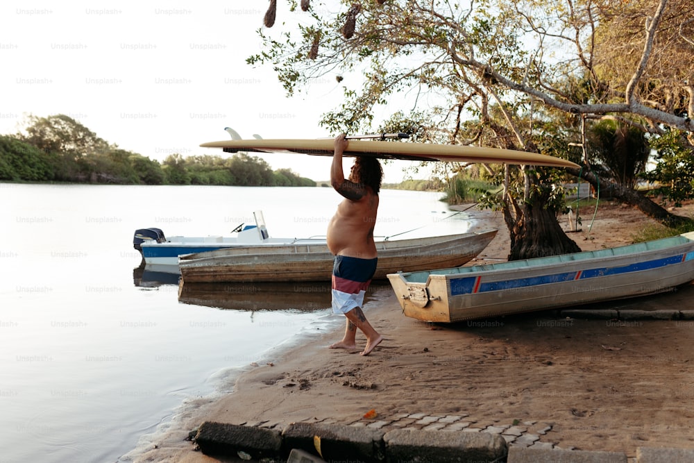 um homem carregando uma prancha de surf sobre a cabeça perto de um corpo de água