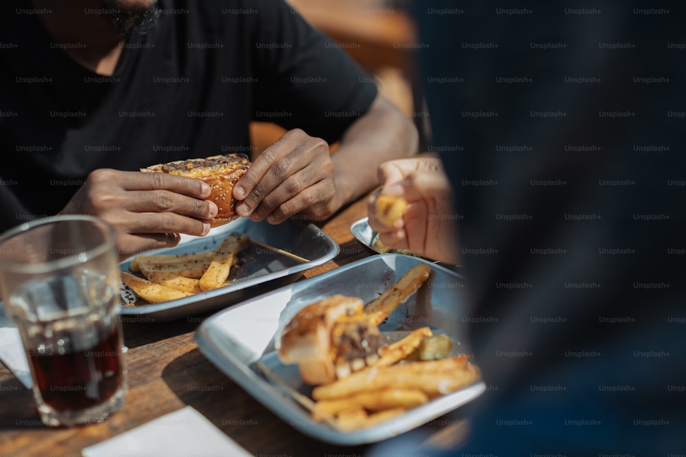 um homem comendo um sanduíche e batatas fritas em uma mesa