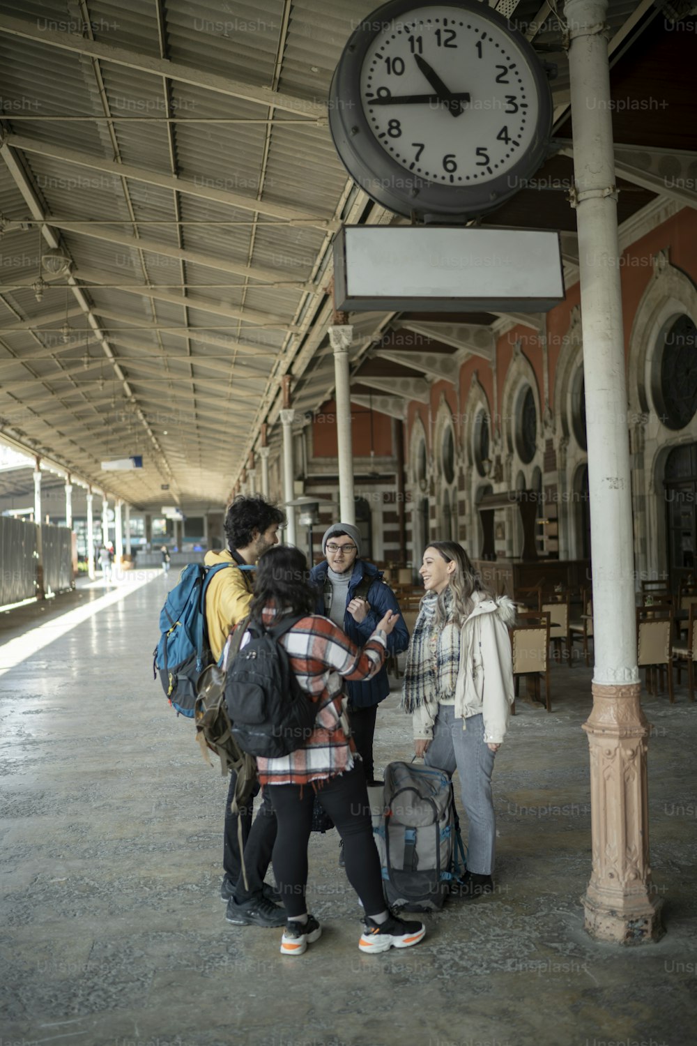 um grupo de pessoas em pé sob um relógio em uma estação de trem