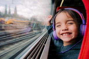 uma garotinha com fones de ouvido ao olhar para fora de uma janela de trem