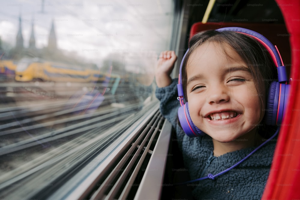 a little girl with headphones on looking out of a train window