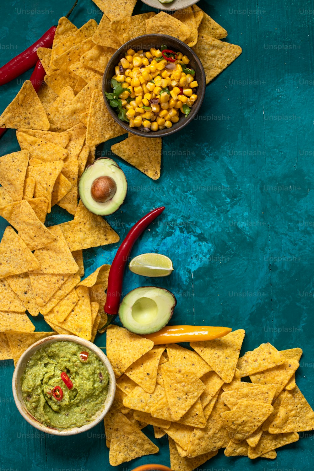 chips, guacamole, and salsa are arranged on a blue surface