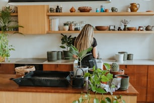 a woman standing in a kitchen next to a plant
