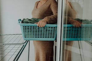 a woman holding a laundry basket in front of a window