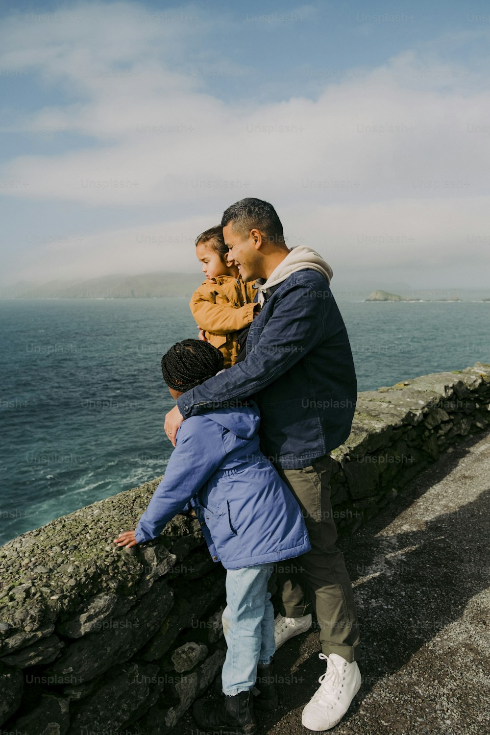 a man and two boys standing on a stone wall by the ocean