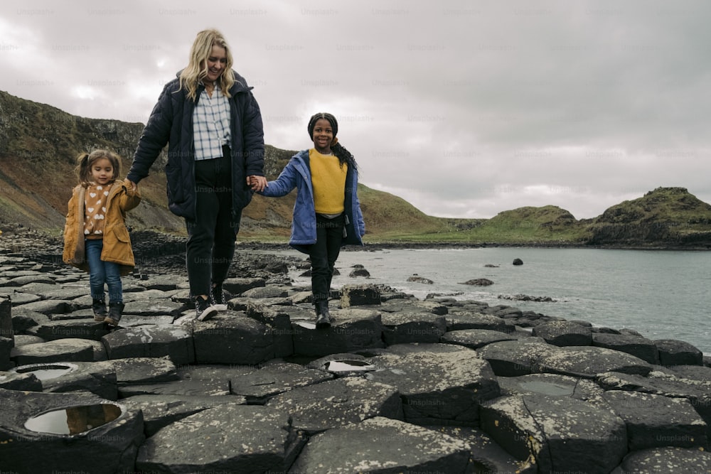 a woman and two children walking along a rocky shore