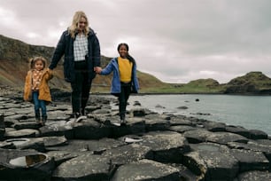 a woman and two children walking along a rocky shore