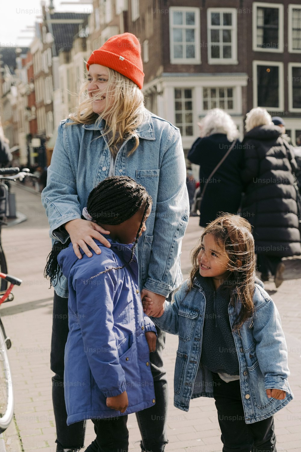 a woman standing next to two children on a sidewalk
