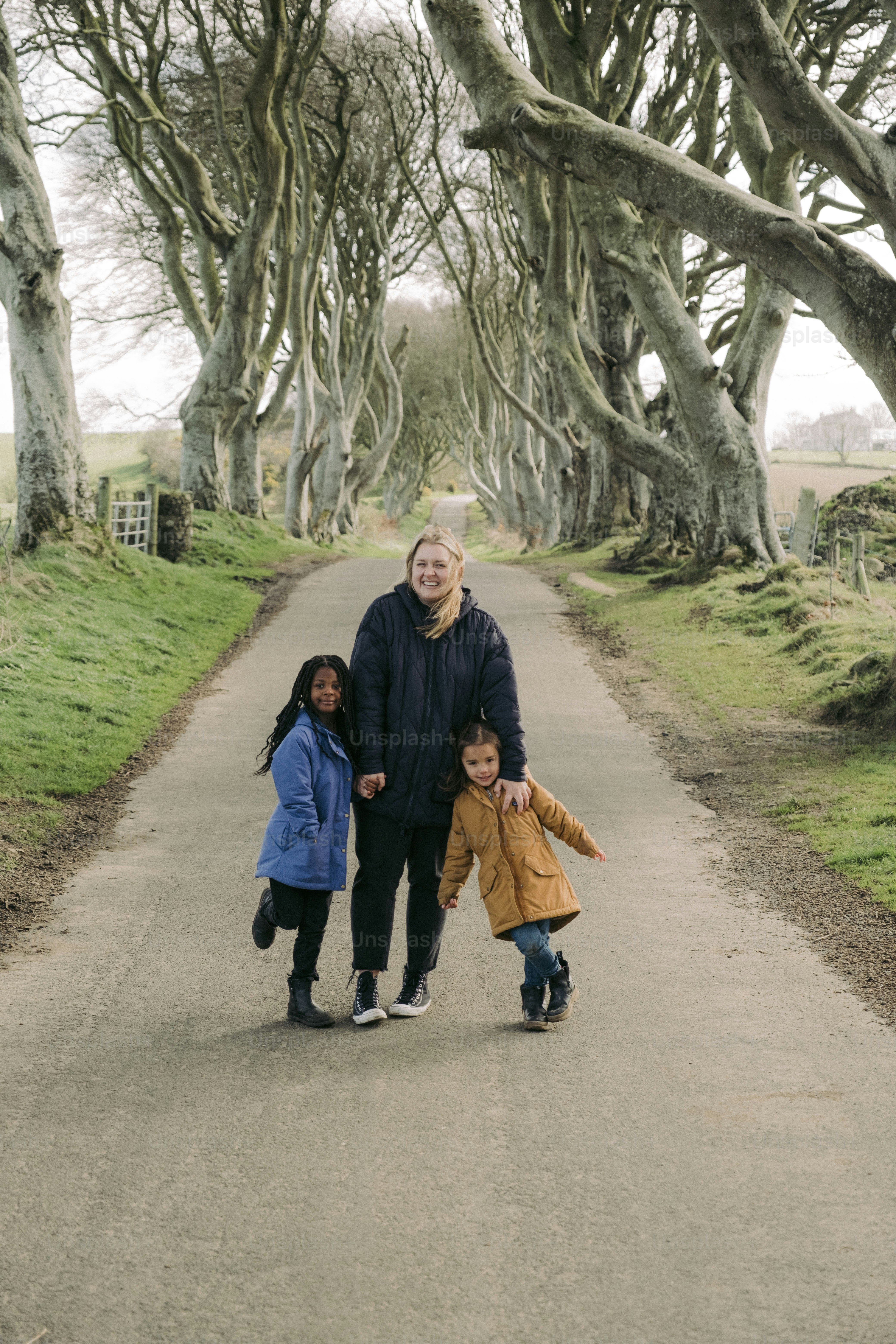 a woman and two children walking down a road lined with trees
