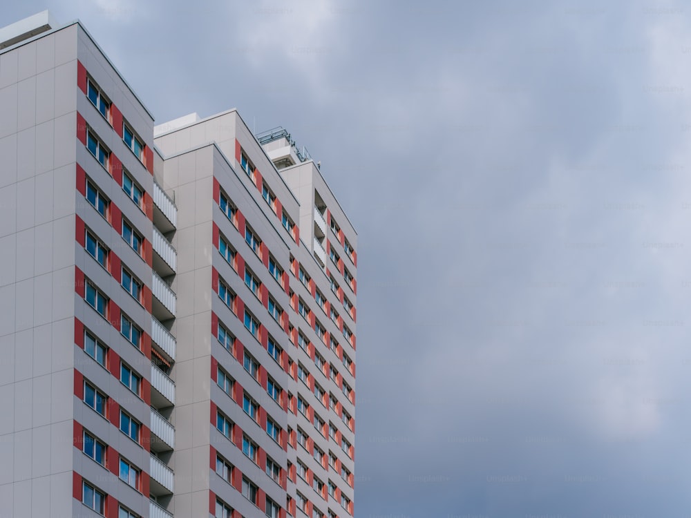 um edifício alto branco e vermelho ao lado de um céu nublado