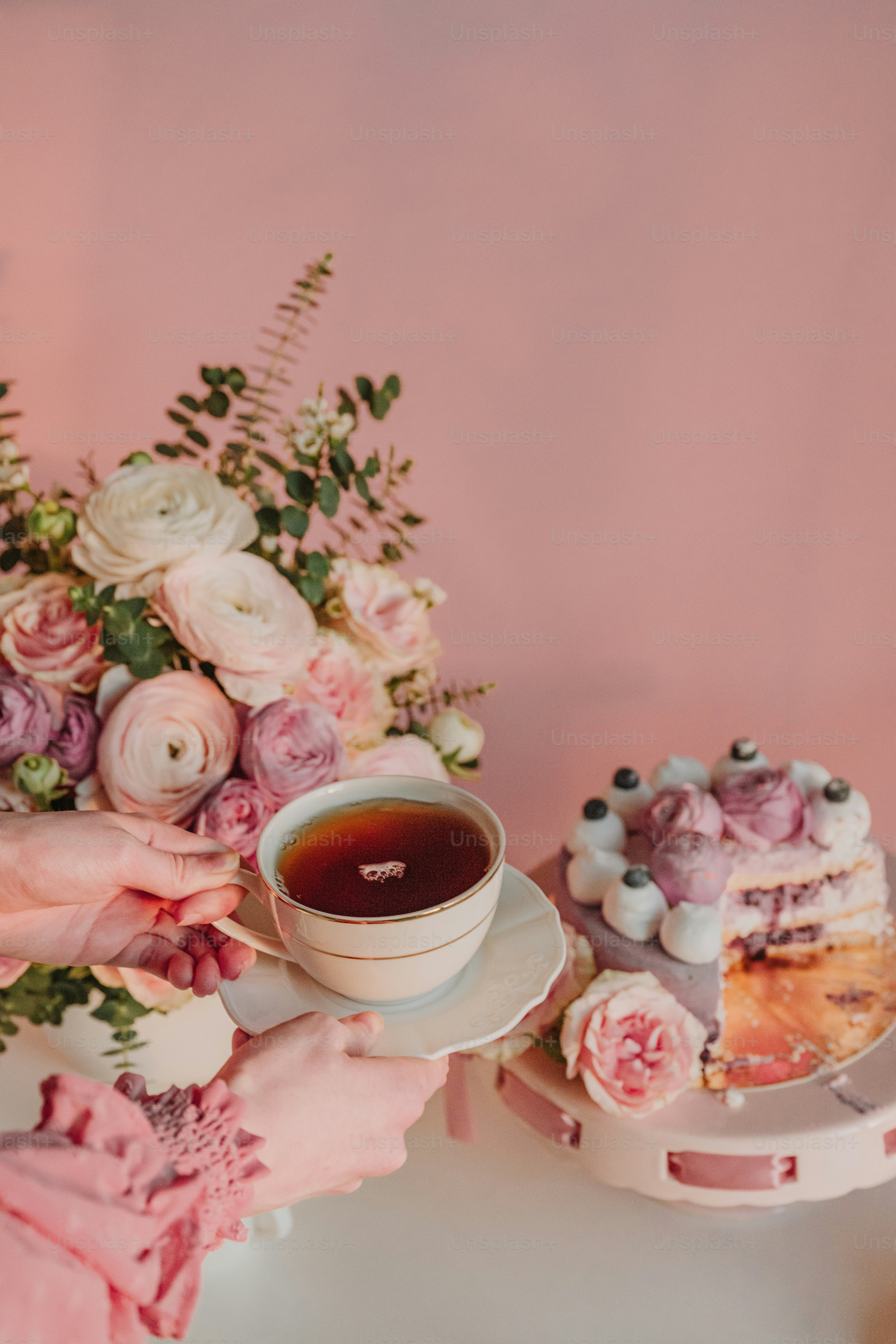 a woman holding a cup of tea next to a piece of cake
