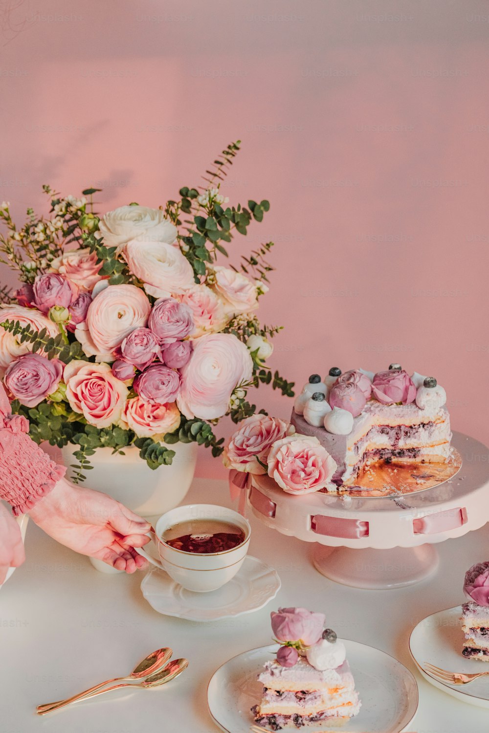uma mesa branca coberta com bolos e um vaso cheio de flores