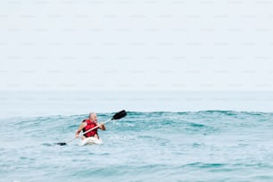Un uomo in un giubbotto di salvataggio rosso che pagaia un kayak nell'oceano