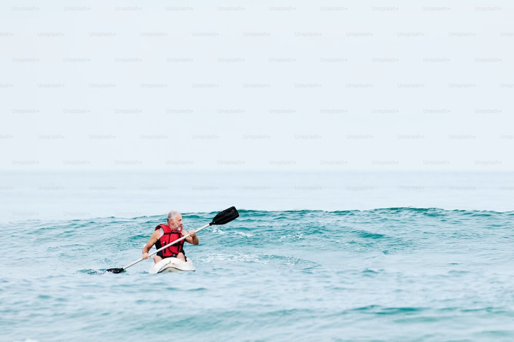Un hombre con un chaleco salvavidas rojo remando en un kayak en el océano