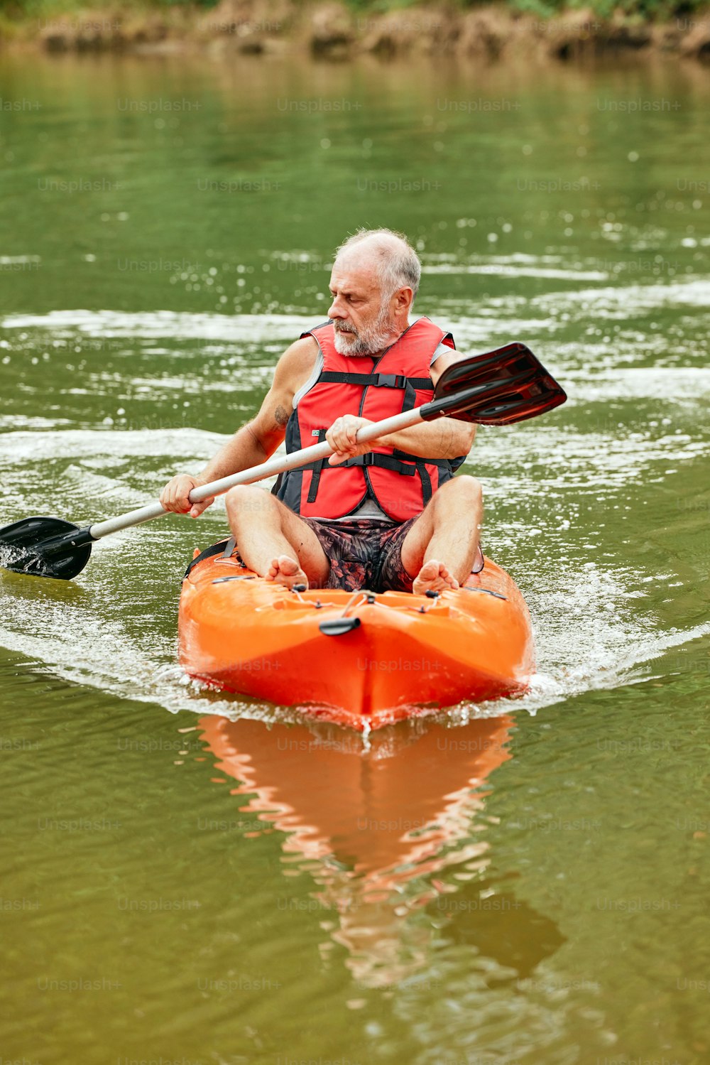Un uomo in un giubbotto di salvataggio arancione che pagaia un kayak