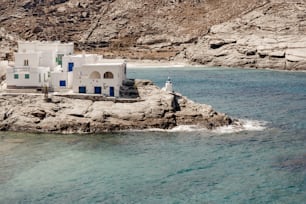 Un edificio bianco seduto sulla cima di una scogliera rocciosa accanto a uno specchio d'acqua