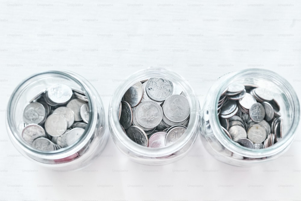 three glass jars filled with coins on a white surface