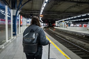 una persona con una valigia in attesa in una stazione ferroviaria