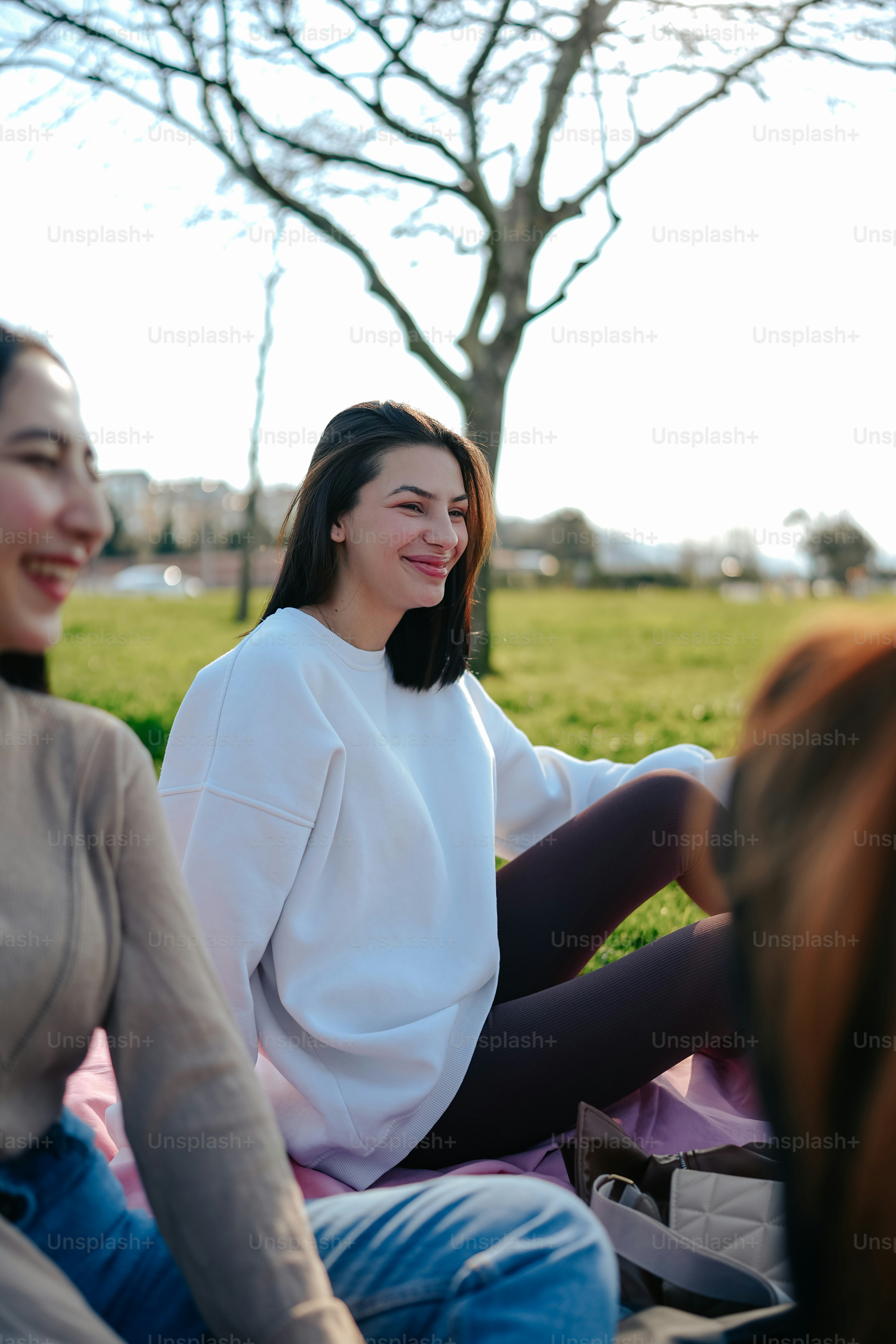 two women sitting on a blanket in a park