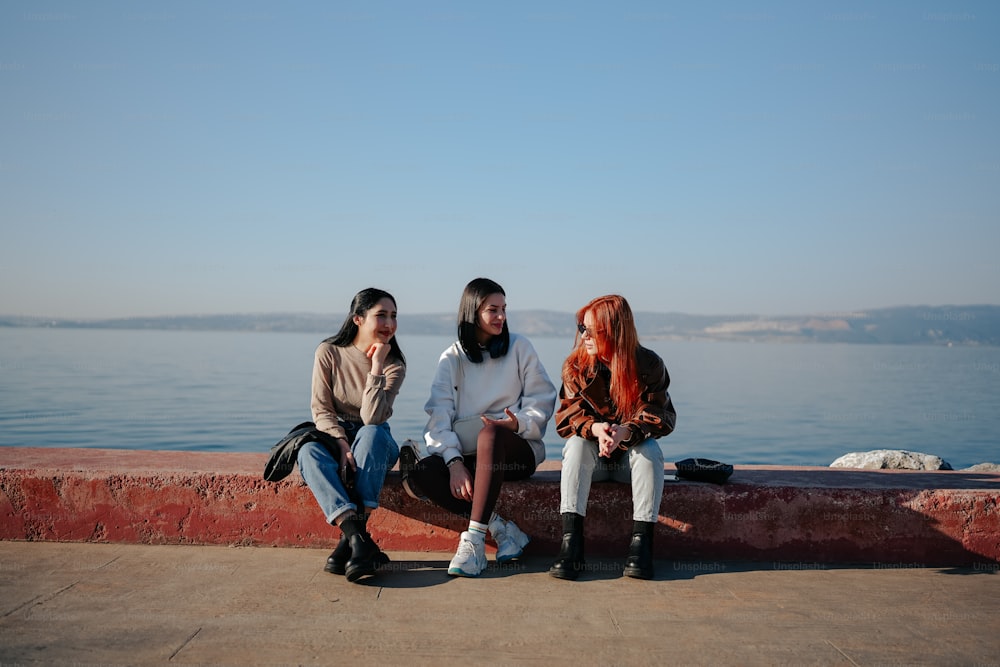 Tres mujeres sentadas en una pared cerca del agua