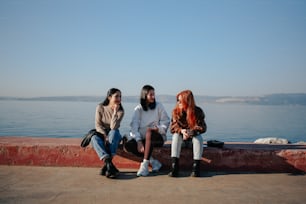 three women sitting on a wall near the water